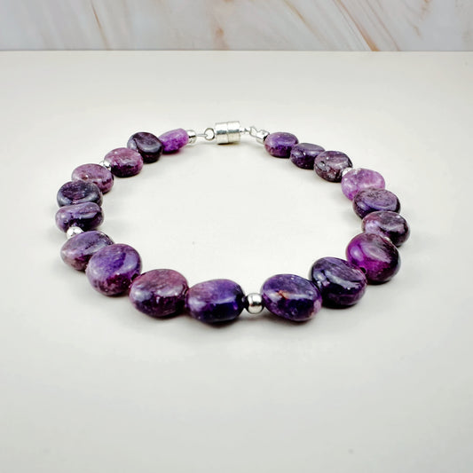 Purple beaded bracelet on a white surface with a light wood background