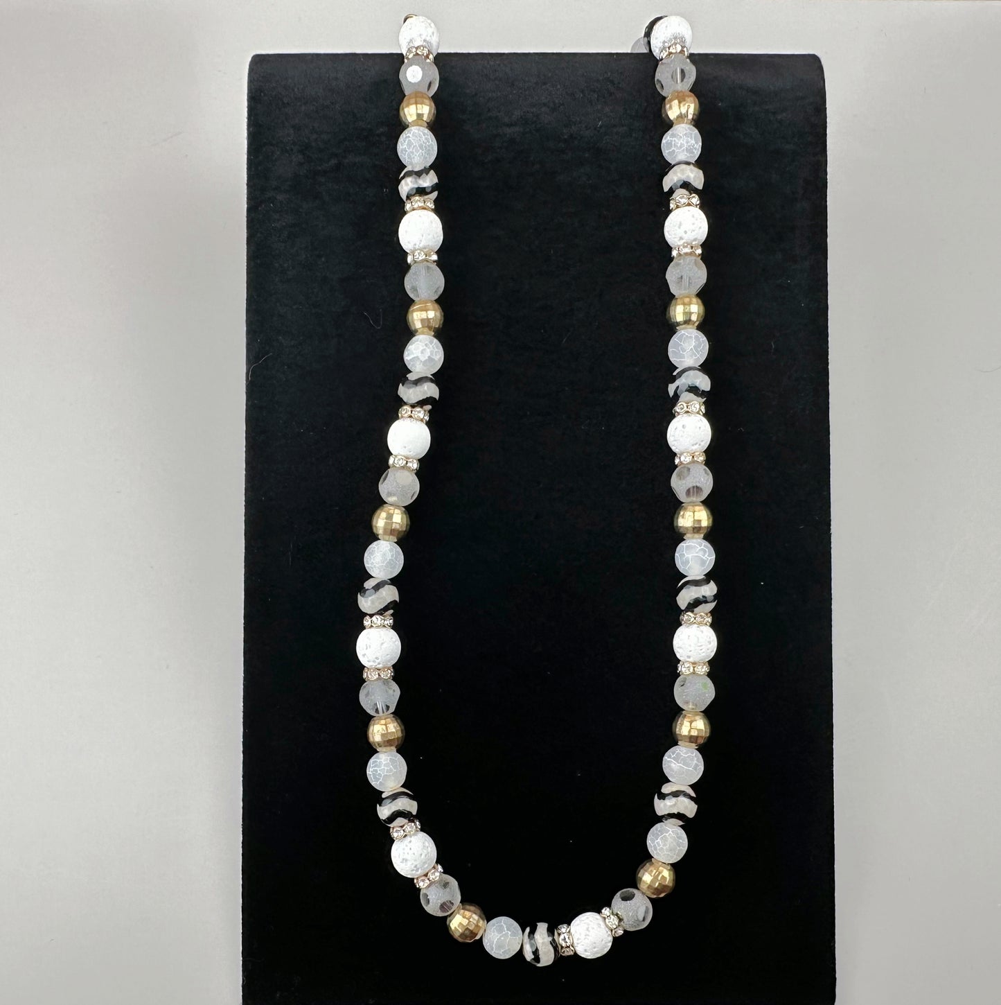 Necklace with white and gold beads on a black stand