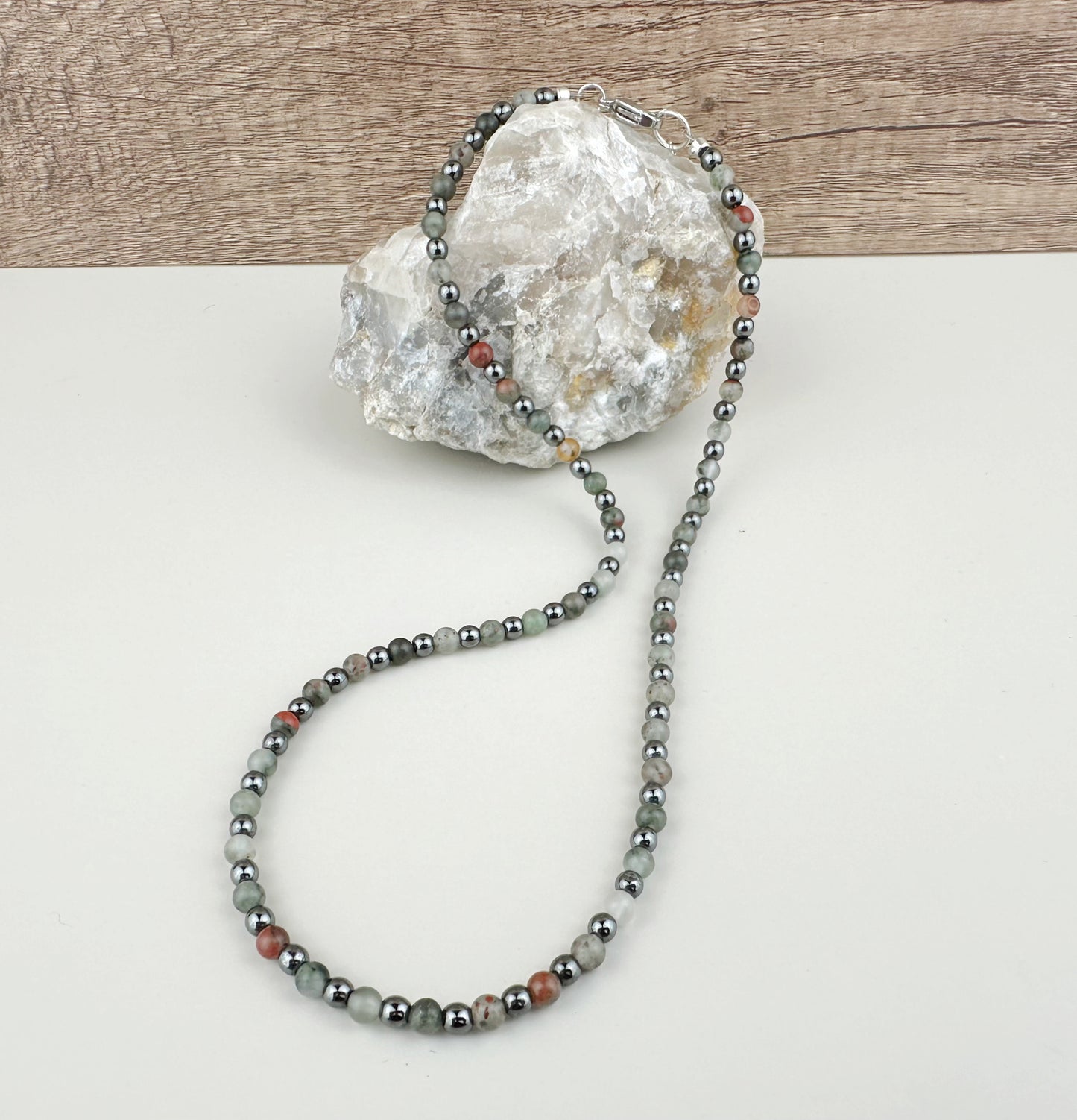 Necklace with gray beads draped over a decorative rock on a light surface.