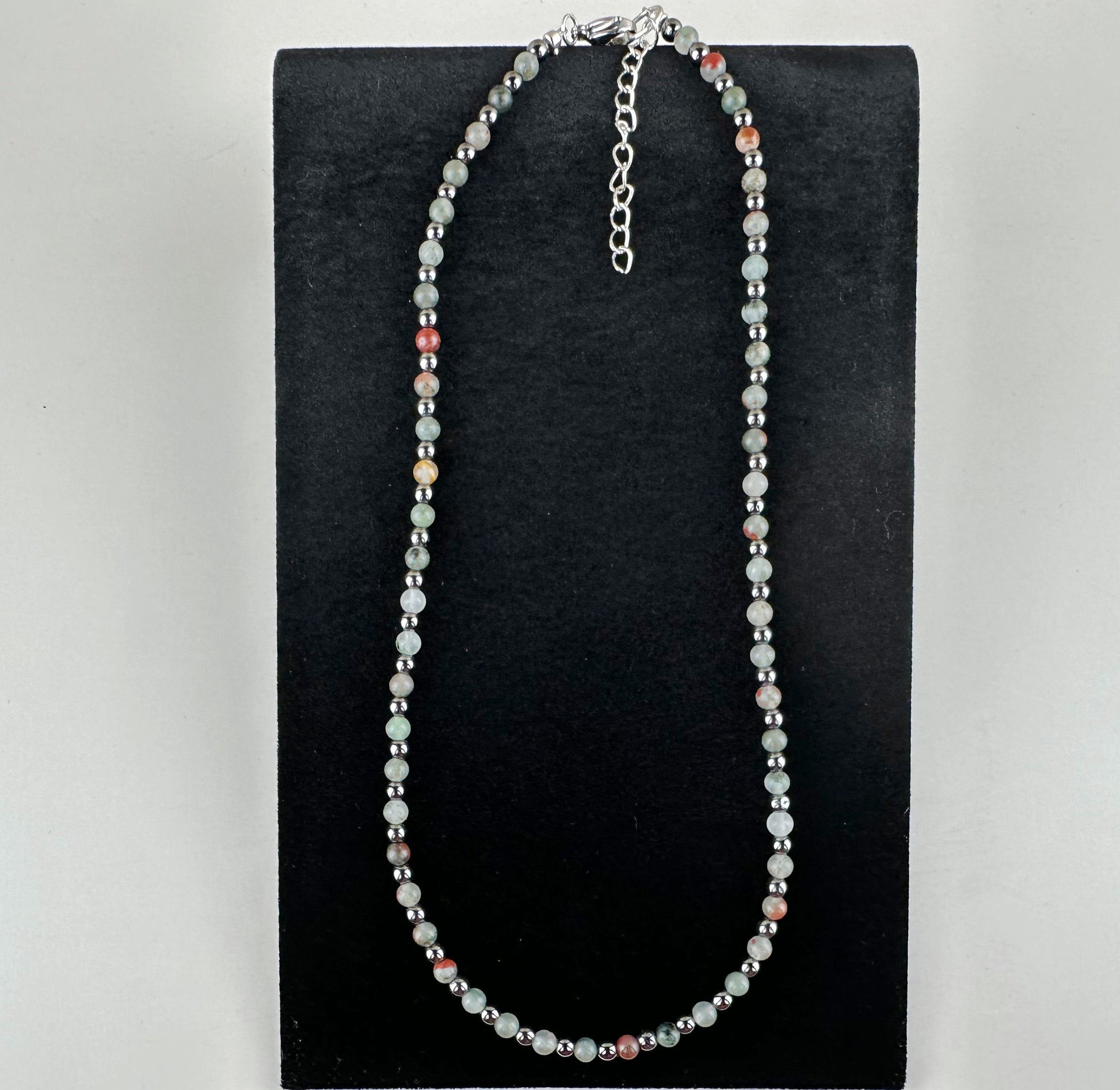 Beaded necklace on a black stand with a white background
