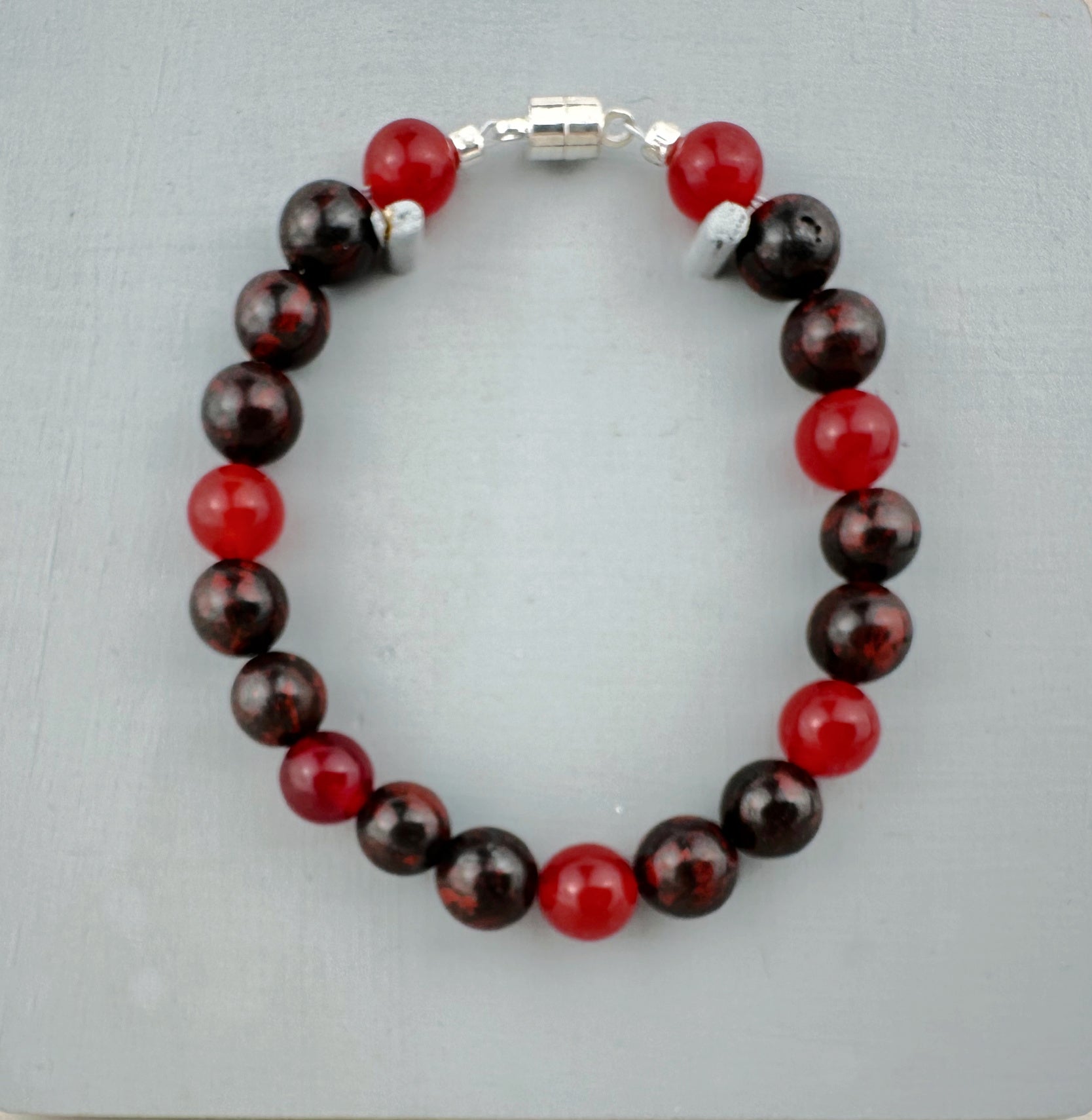 Beaded bracelet with red and brown beads on a light gray background