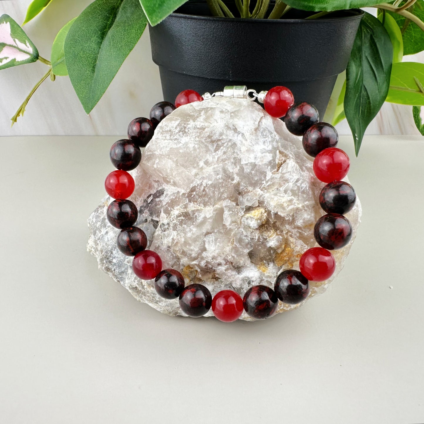 Bracelet with red and black beads on a crystal rock with a plant in the background