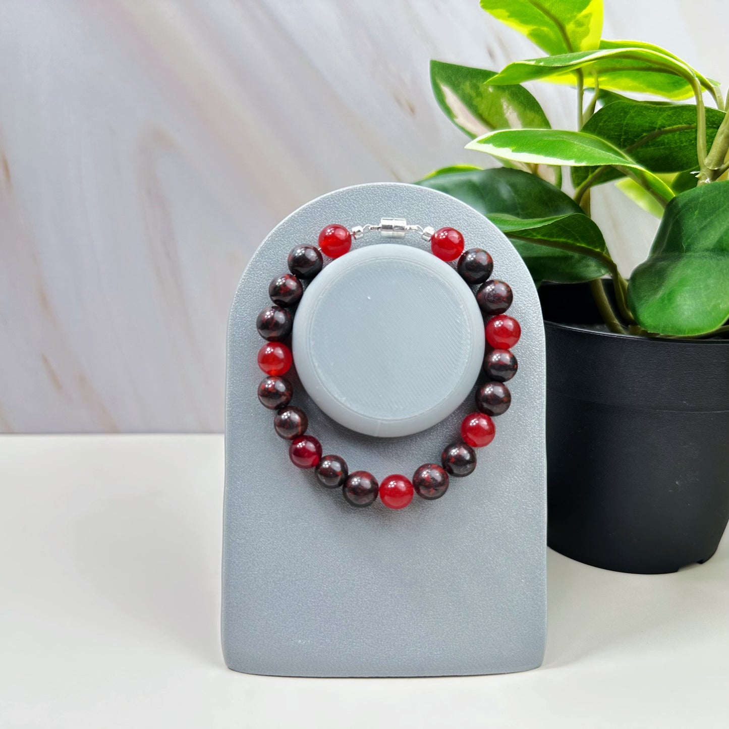 Two beaded bracelets on a gray stand with a plant in the background