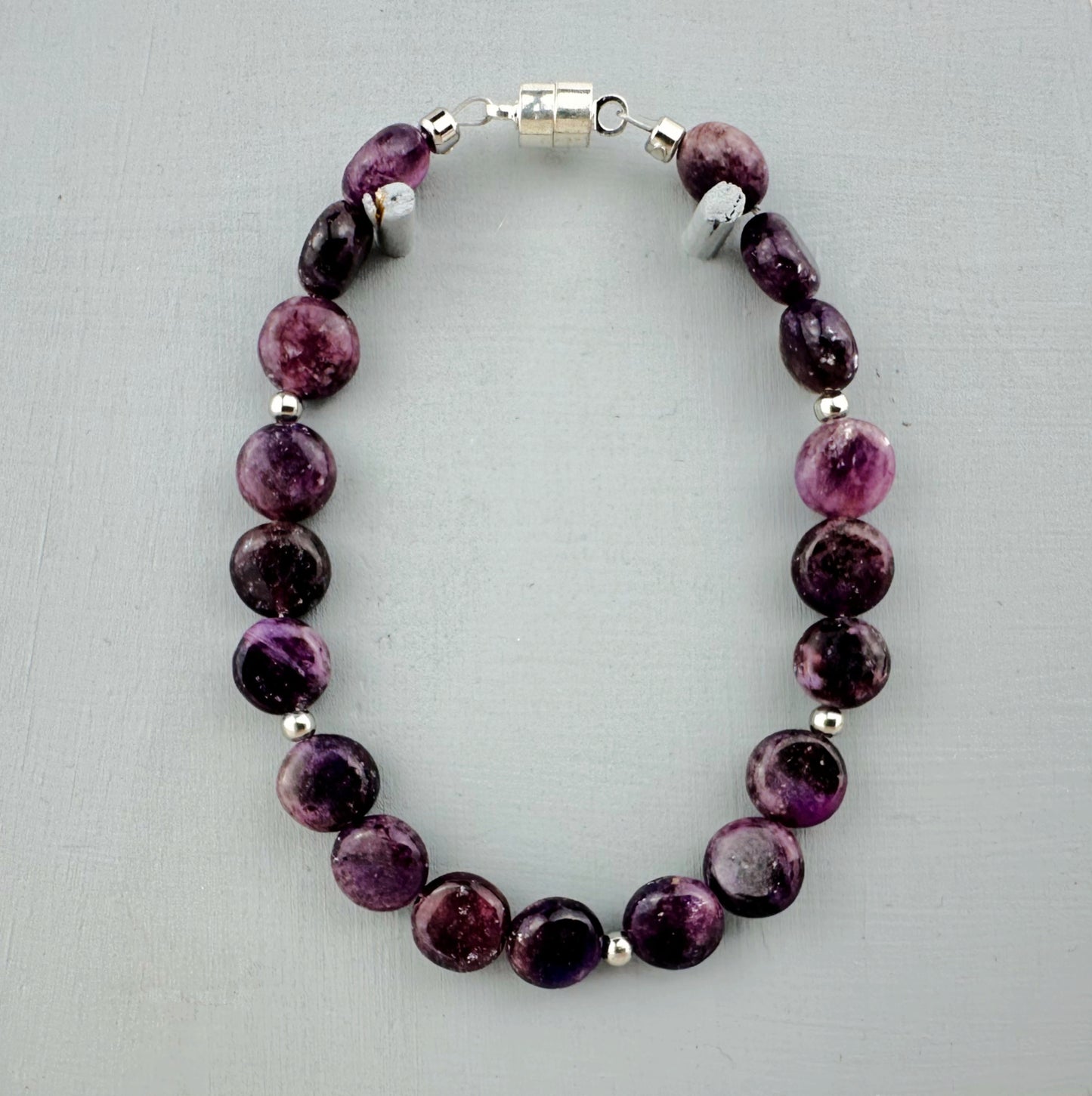 Purple beaded bracelet with silver accents on a light gray background