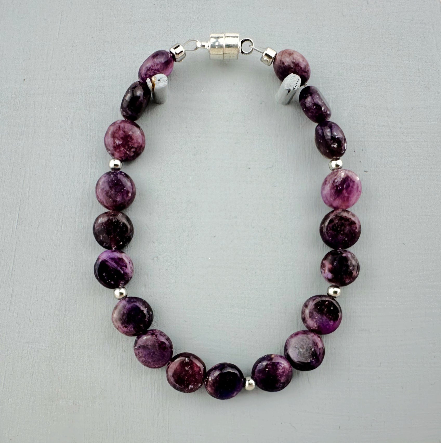 Purple beaded bracelet with silver accents on a light gray background