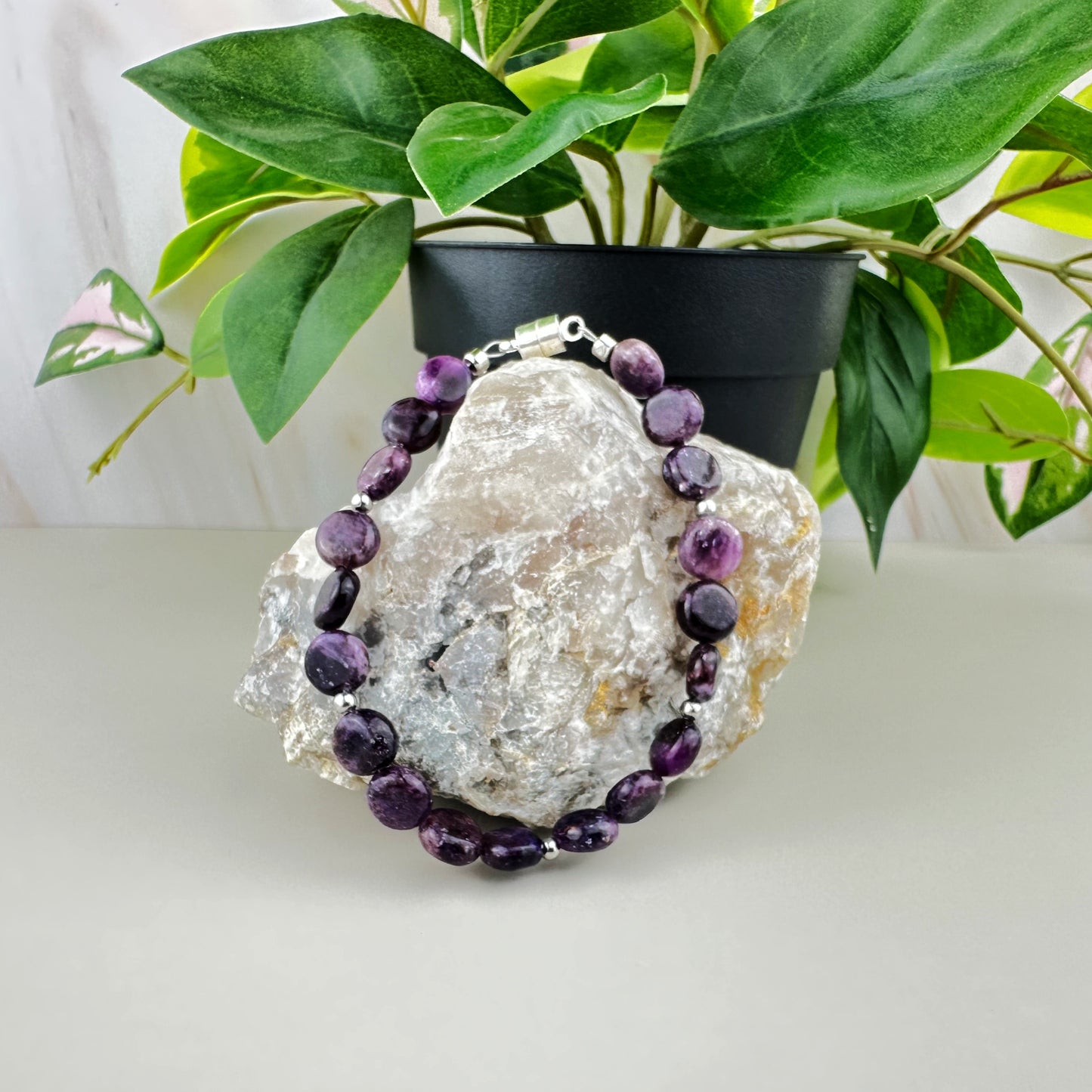 Purple beaded necklace on a decorative rock with a plant in the background