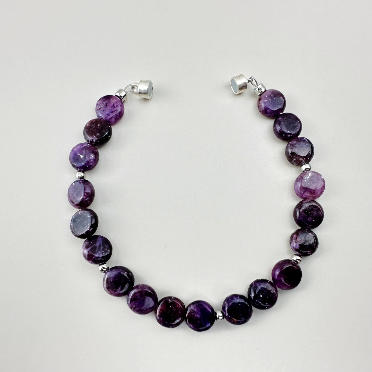 Purple beaded bracelet with silver clasps on a light gray background