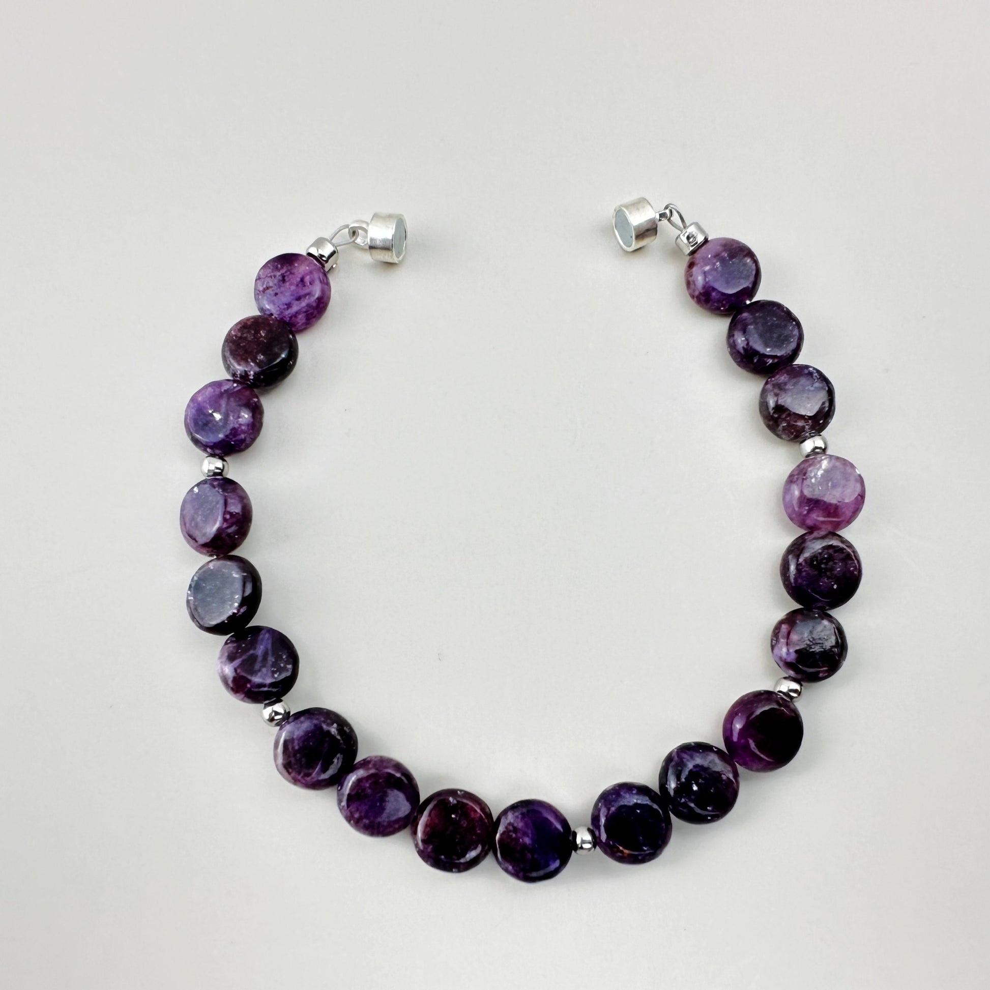 Purple beaded bracelet with silver clasps on a light gray background