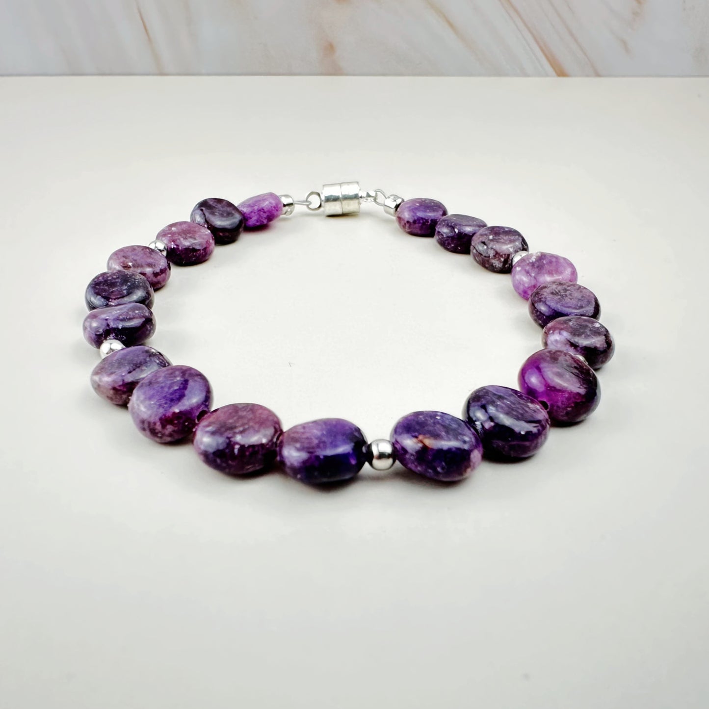 Purple beaded bracelet on a white surface with a light wood background
