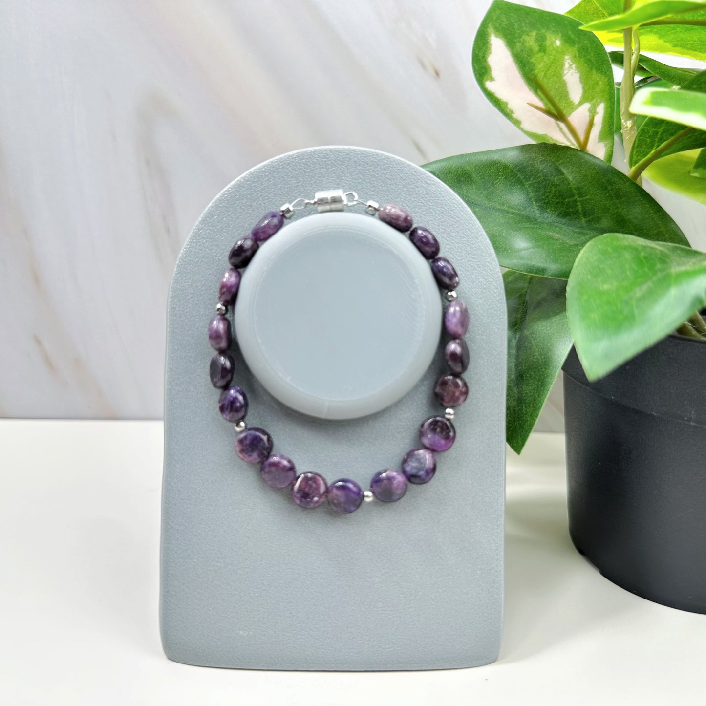 Purple beaded bracelet on a gray stand with a plant in the background