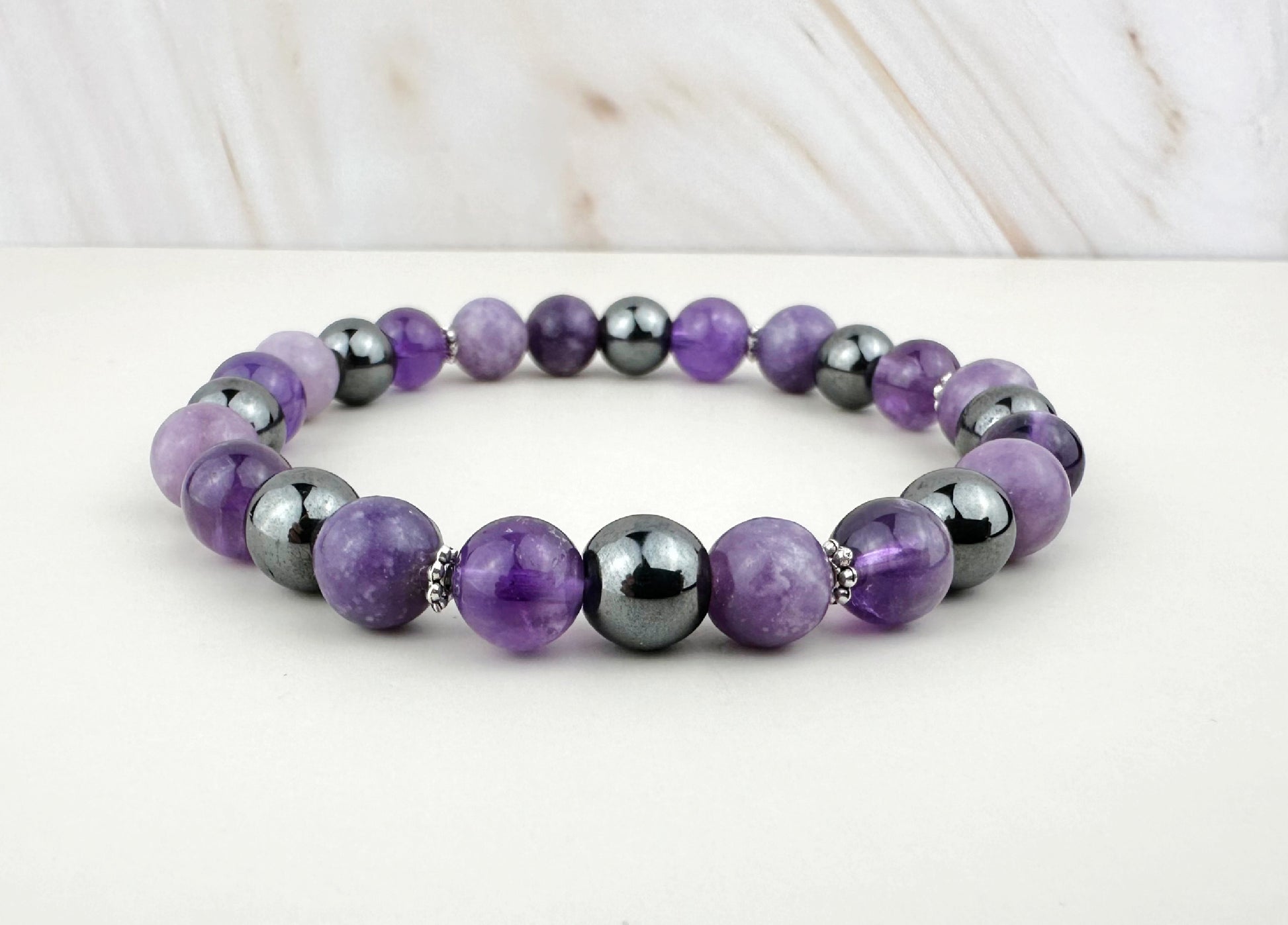 Purple and gray beaded bracelet on a white surface with a light wood background