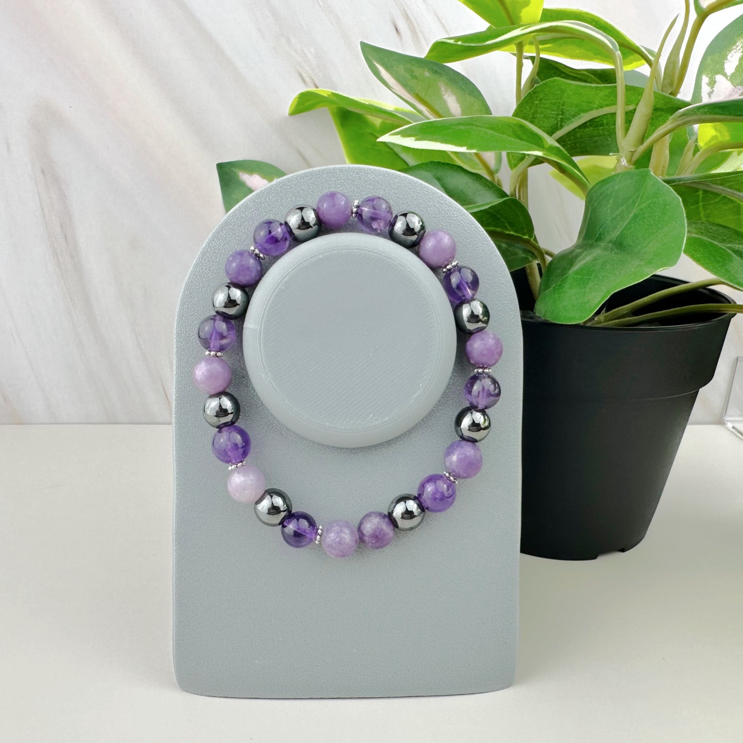 Purple beaded bracelet on a gray stand with a plant in the background