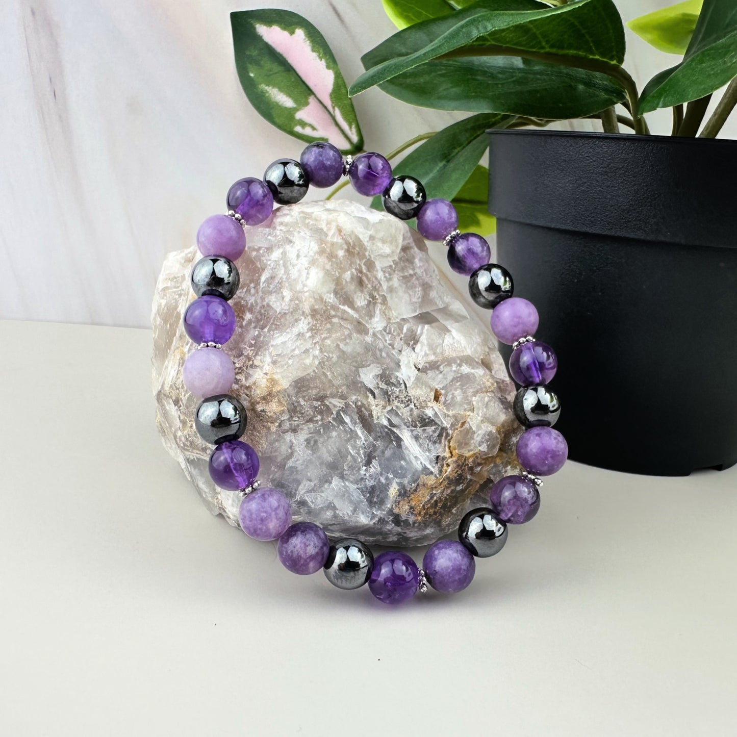 Purple and black beaded bracelet on a rock with a plant in the background