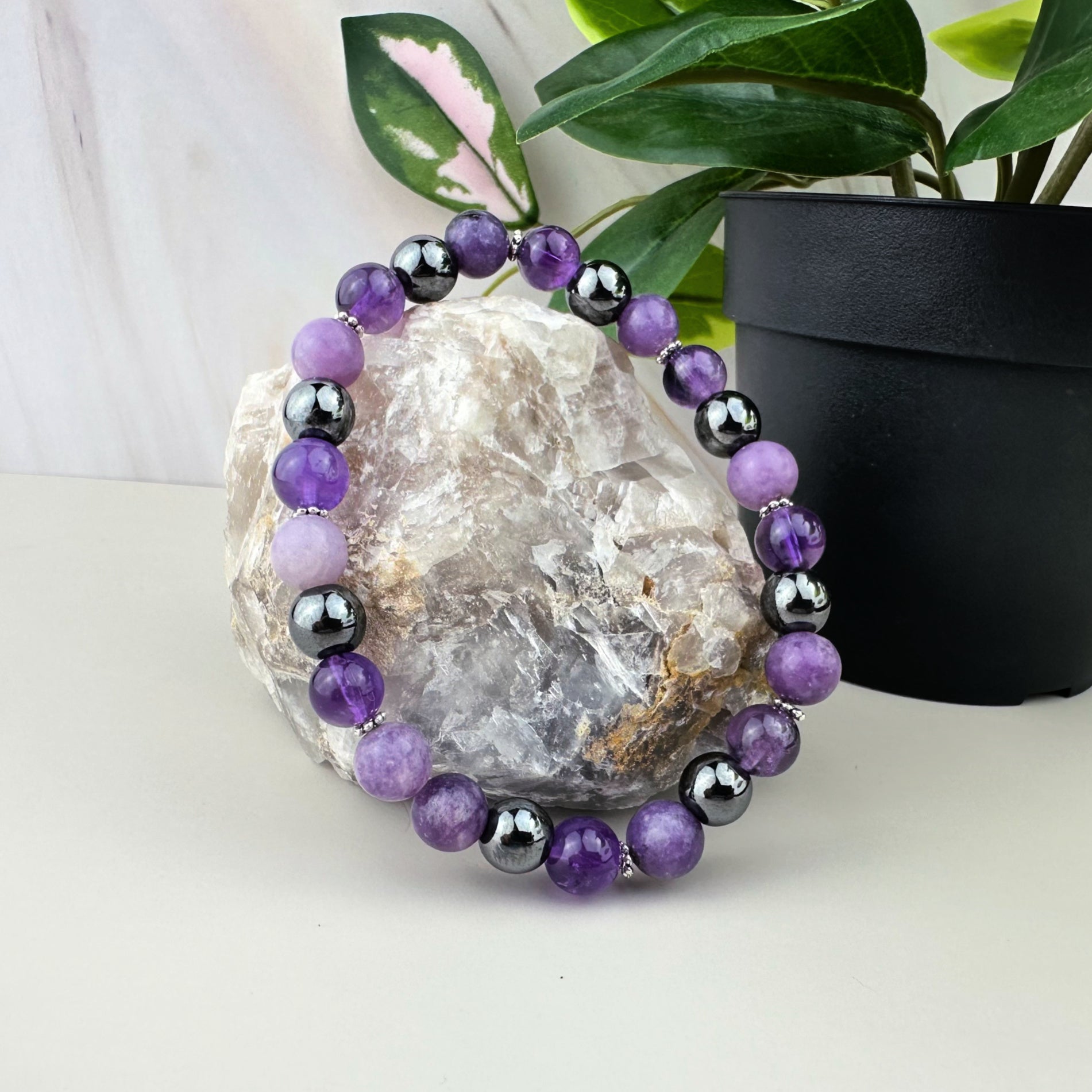 Purple and black beaded bracelet on a rock with a plant in the background