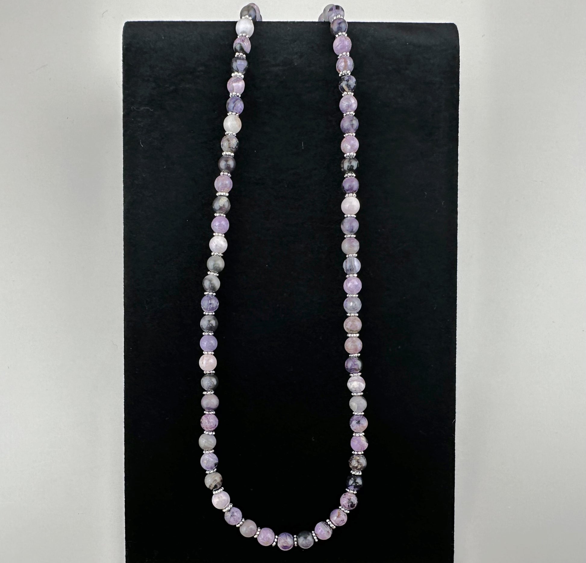 Necklace with multicolored beads on a black stand against a gray background