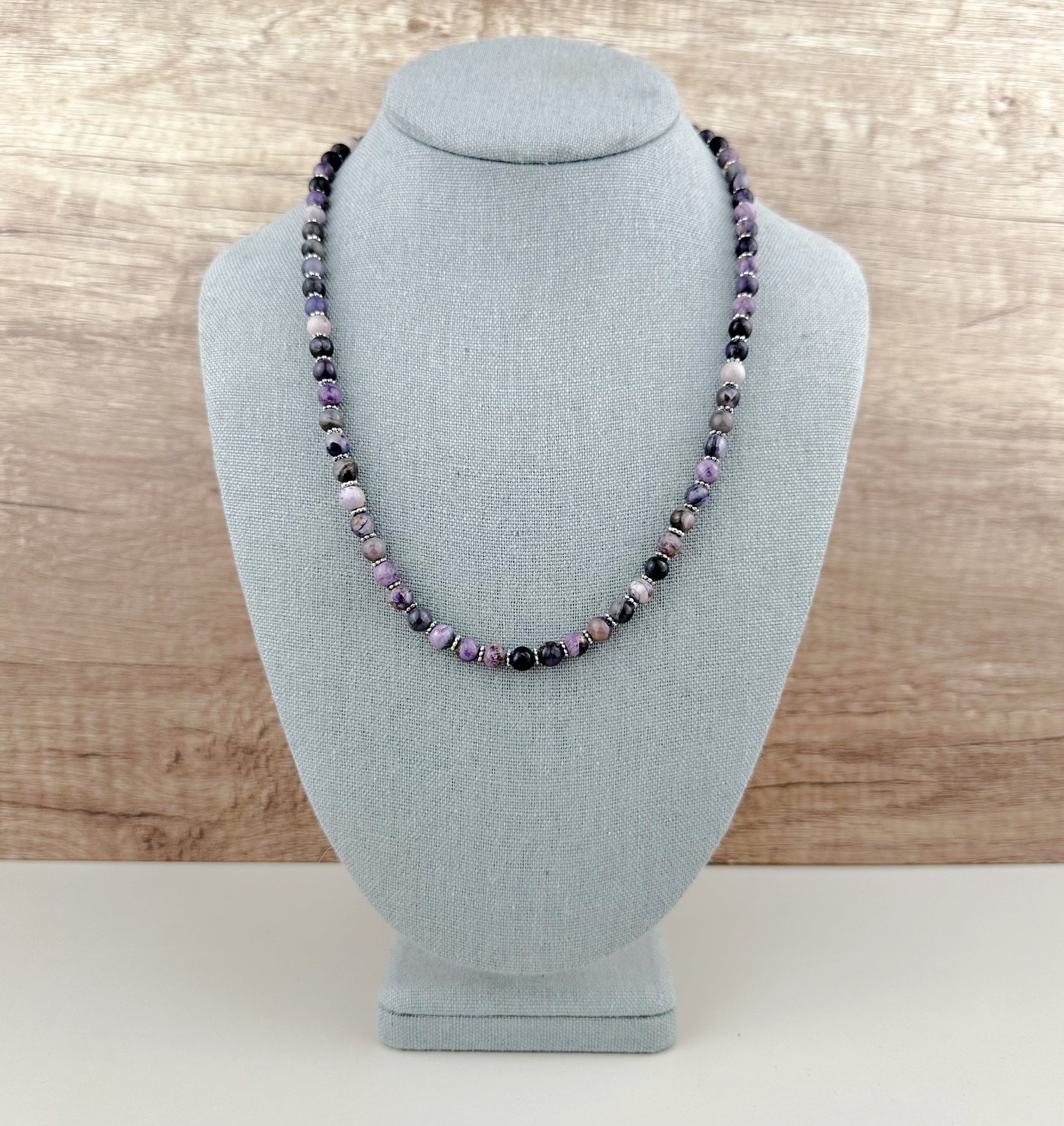 Necklace with purple and black beads on a gray bust against a wooden background