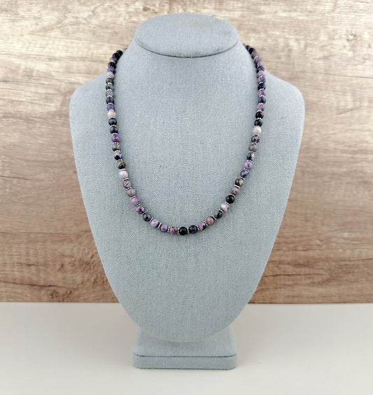 Necklace with purple and black beads on a gray bust against a wooden background