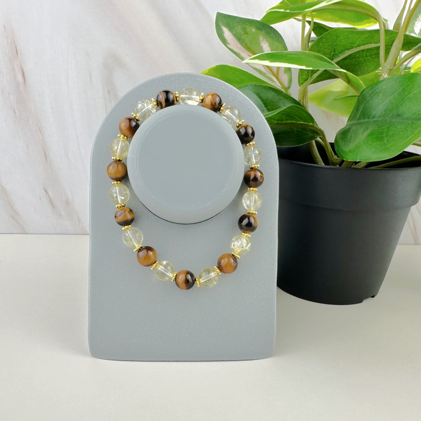 Beaded bracelet on a gray stand with a plant in the background