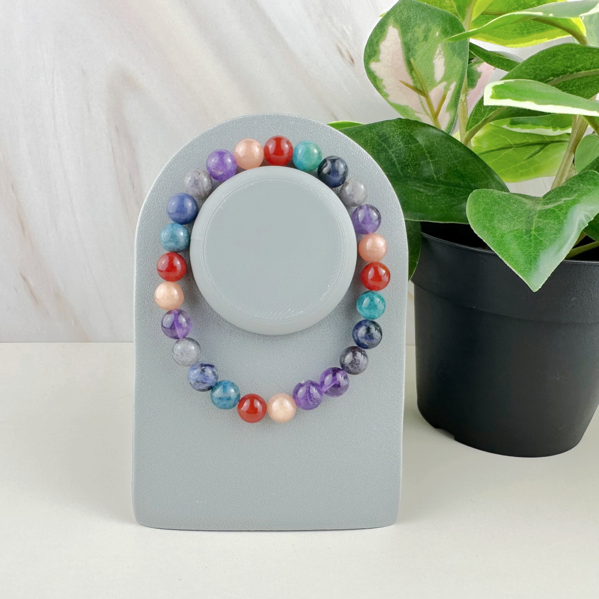 Colorful beaded bracelet on a gray stand with a plant in the background