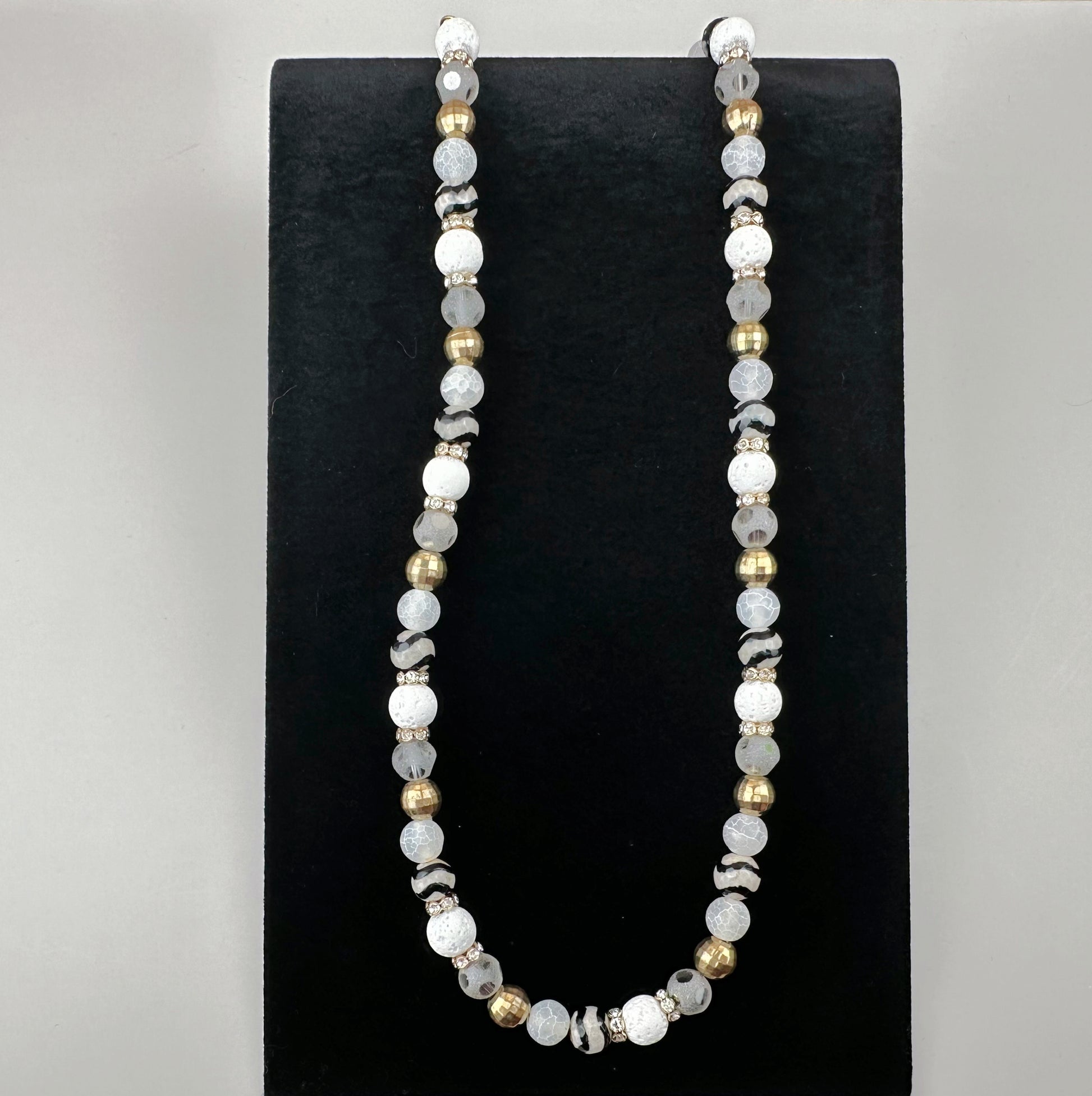 Necklace with white and gold beads on a black stand