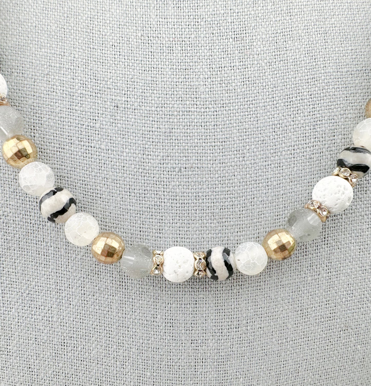Beaded bracelet with white, gold, and black beads on a gray background