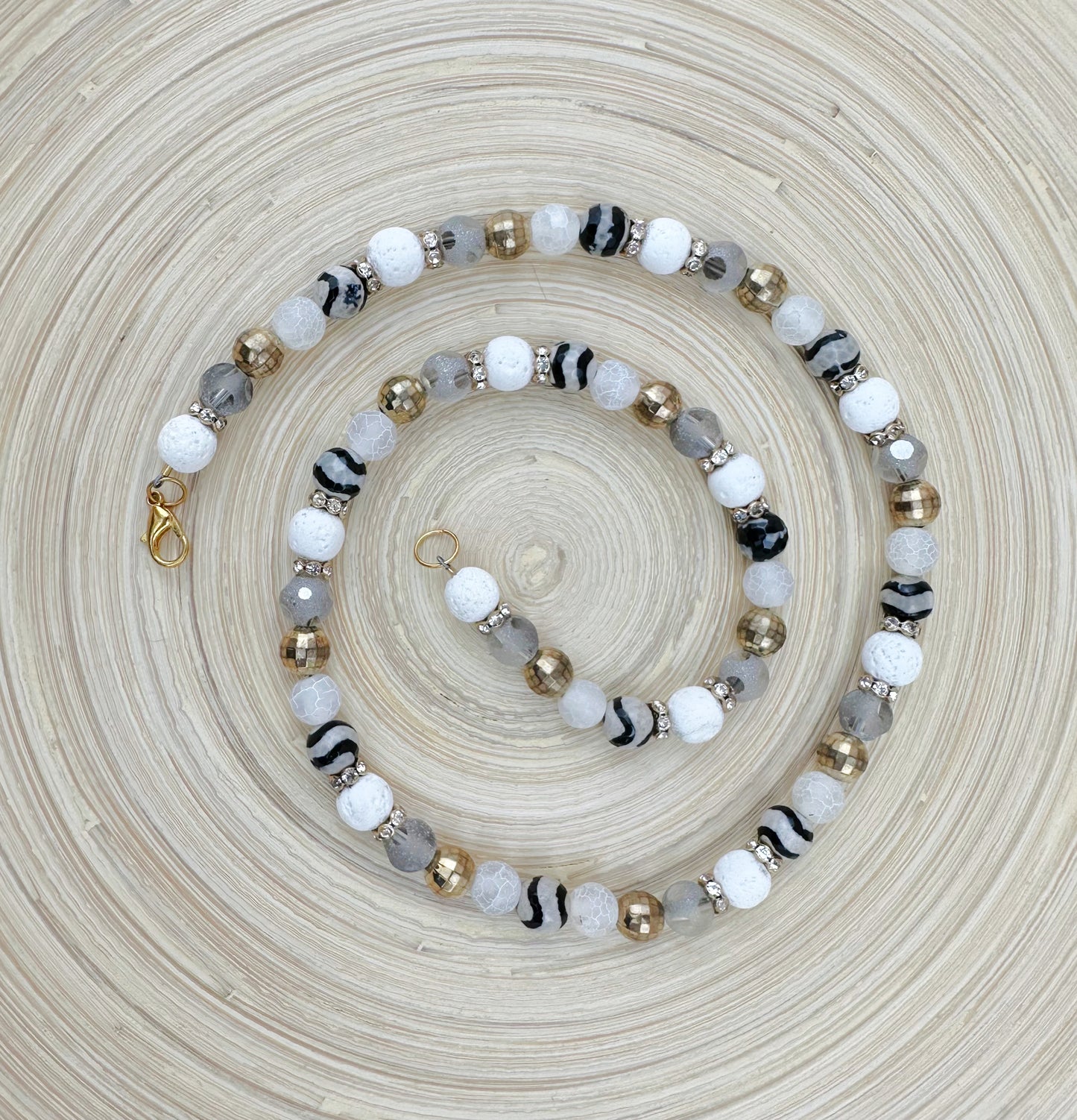 Beaded bracelet with white, black, gray, and gold beads on a textured beige surface