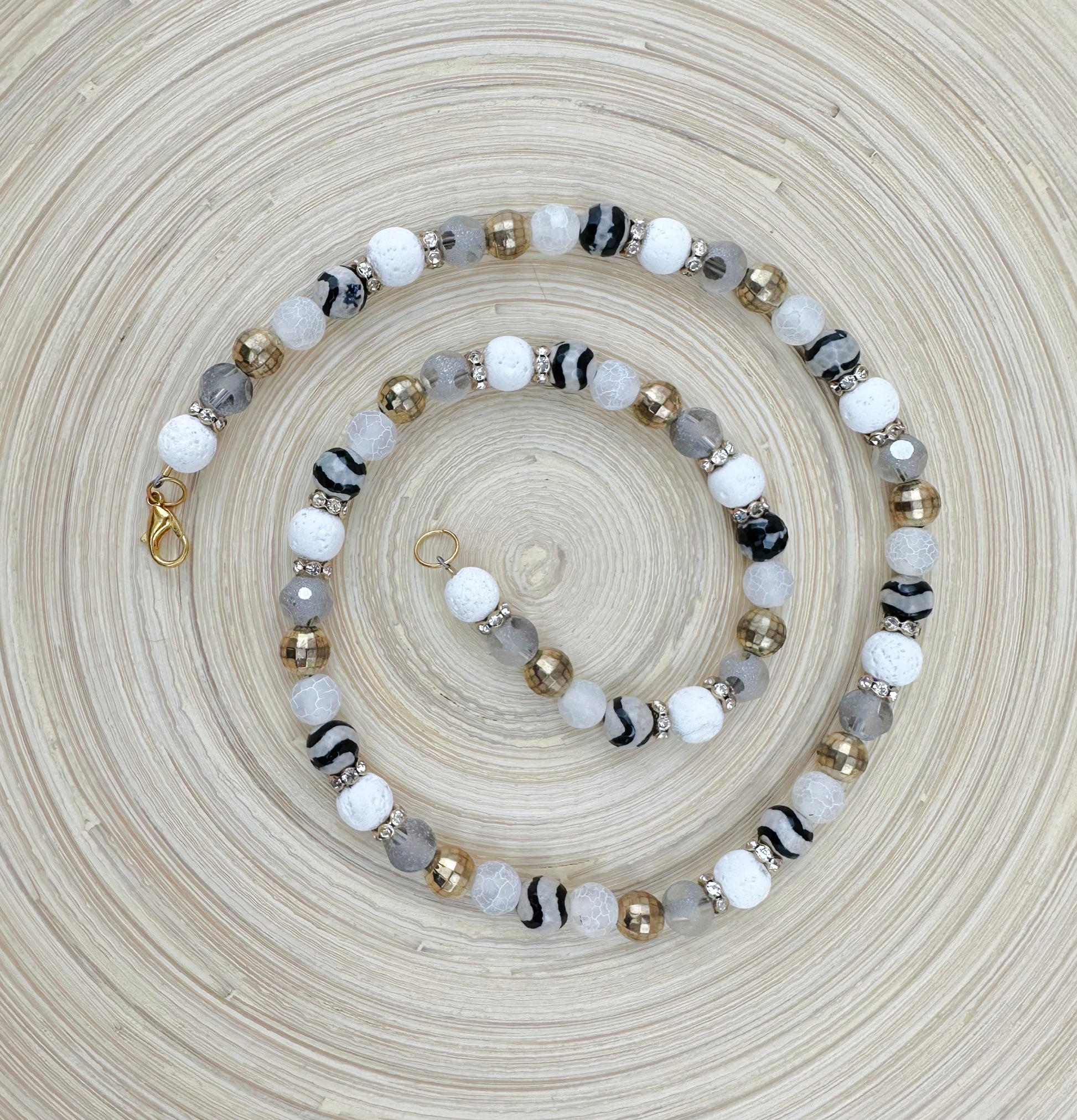 Beaded bracelet with white, black, gray, and gold beads on a textured beige surface