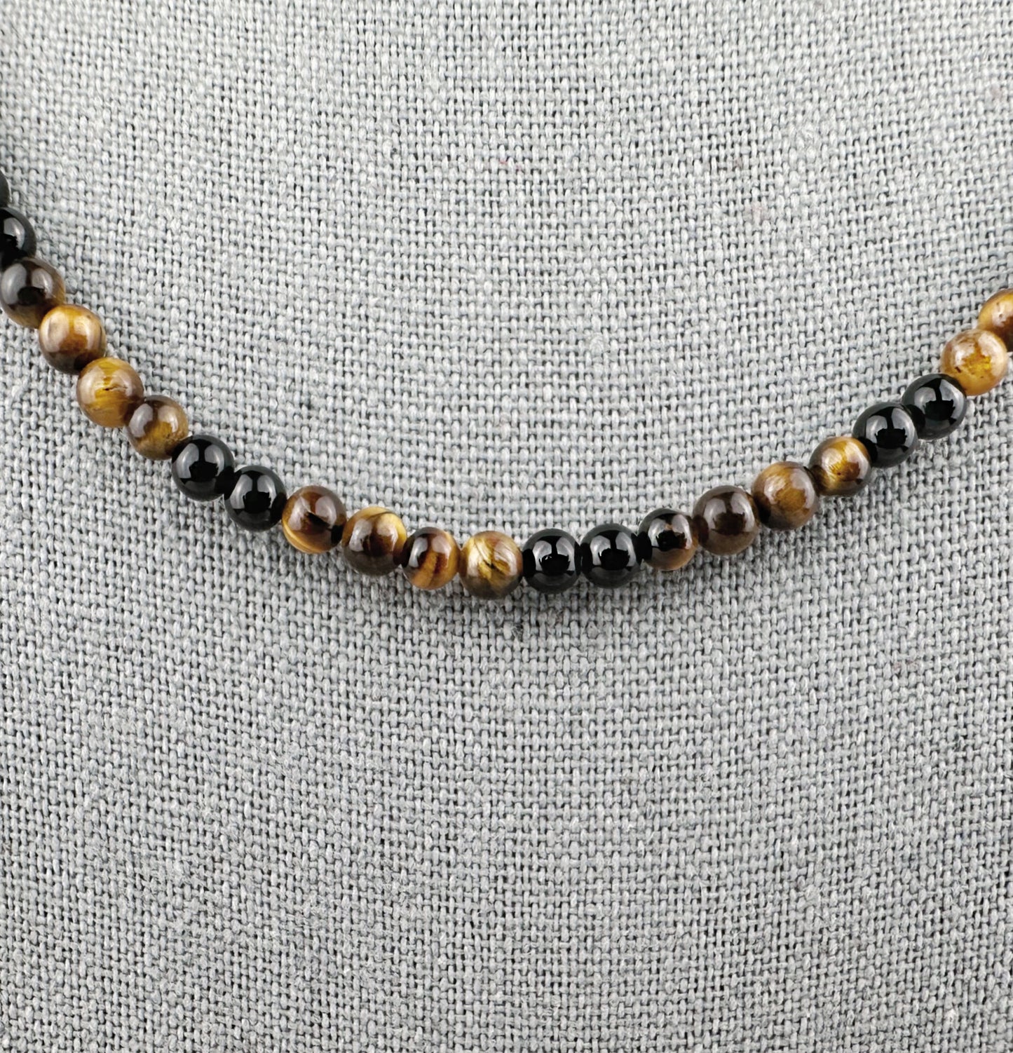 Beaded necklace with black and brown beads on a gray fabric background